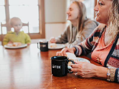 Two women sitting at a table drinking coffee with a baby