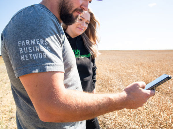 Two farmers standing in field looking at a smartphone